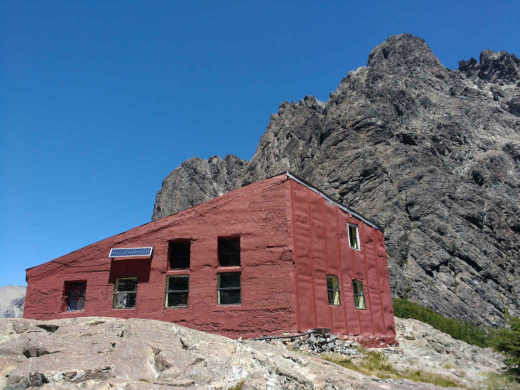 Refugio Italia - Manfredo Segre - en laguna Negra. La imagen tiene al refugio de color terracota en primer plano y al cerro Negro detrás con el fondo de un cielo celeste.