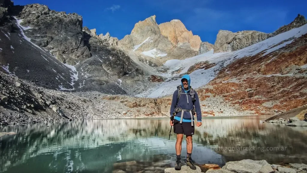 Persona parada mirando al frente con una laguna de deshielo detrás. Al fondo la cara norte del Fitz Roy